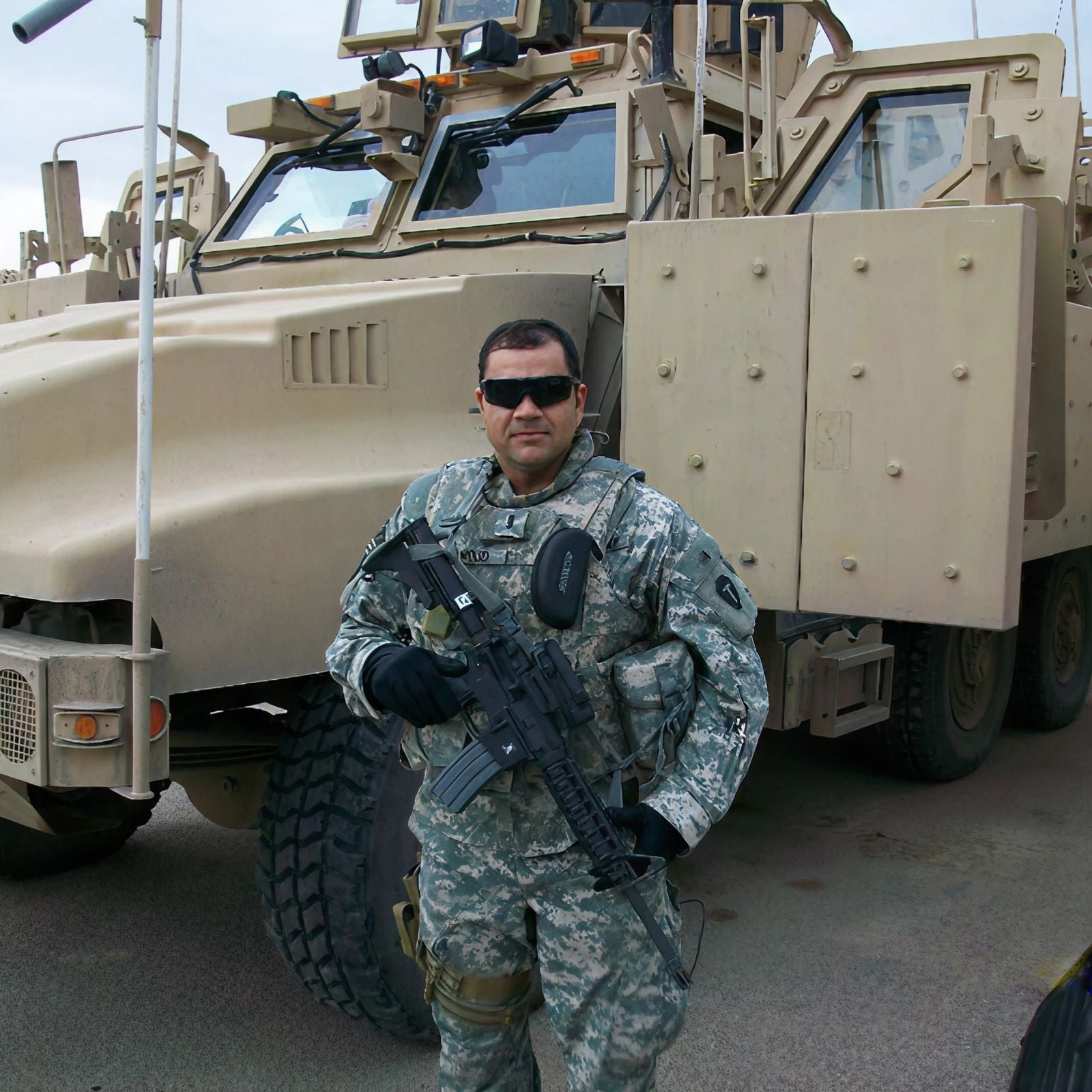 US Military veteran Haidar Hamoud poses in full uniform in front of an armored vehicle. Haidar founded The Beanie Factory to manufacture hats that kept fellow soldiers comfortable during long shirts. The company is veteran-owned and all products are made in the USA.
