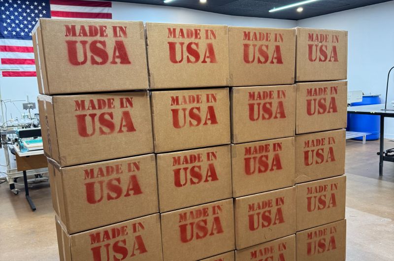 A stack of brown shipping boxes in The Beanie Factory's warehouse, with the American flag in the background. Each box says "Made In USA," as all products made by The Beanie Factory are made in Parma, Ohio.