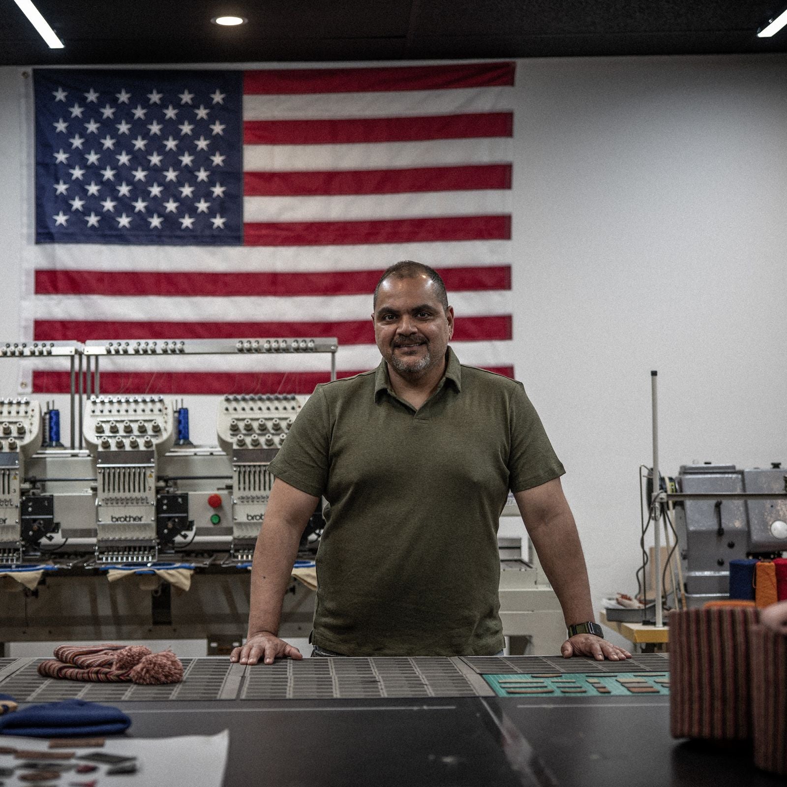 A representative from The Beanie Factory stands in front of an American flag inside the company's production facilities. The Beanie Factory is veteran-owned and proud to make all products in Parma, Ohio, United States.